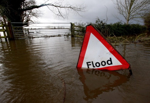 A flood sign is seen in flood waters surrounding farm