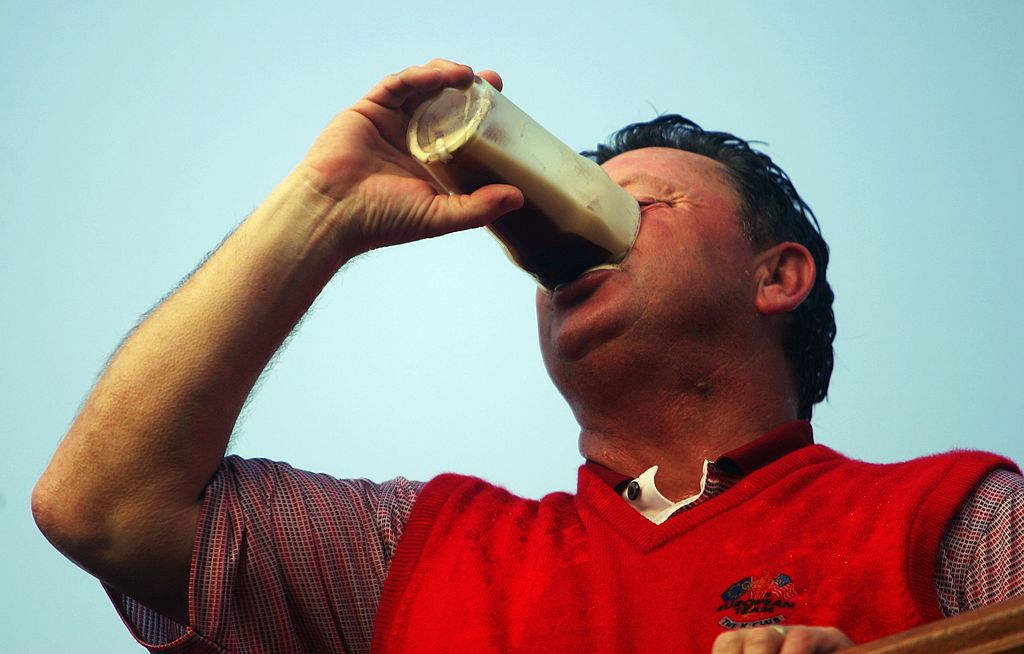 Man drinking tall glass of beer outside