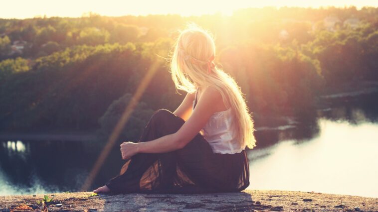 woman sitting on brown surface watching at body of water
