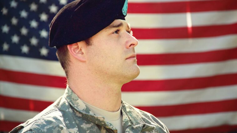 Man Wearing Combat Hat And Top Looking Up Near Flag Of America